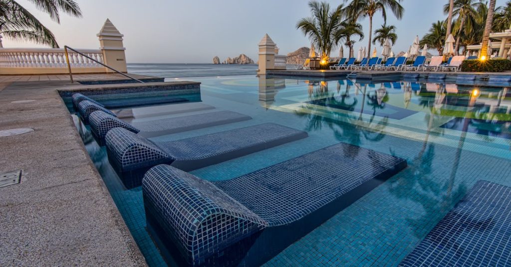 Serene poolside view overlooking the ocean with palm trees and lounge chairs in Cabo San Lucas, capturing tropical tranquility.
